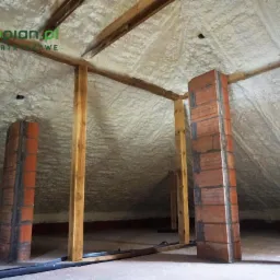 Poddasze z drewnianą konstrukcją i ociepleniem natryskowym pianką, widoczne kominy obłożone cegłą, logo firmy w rogu.