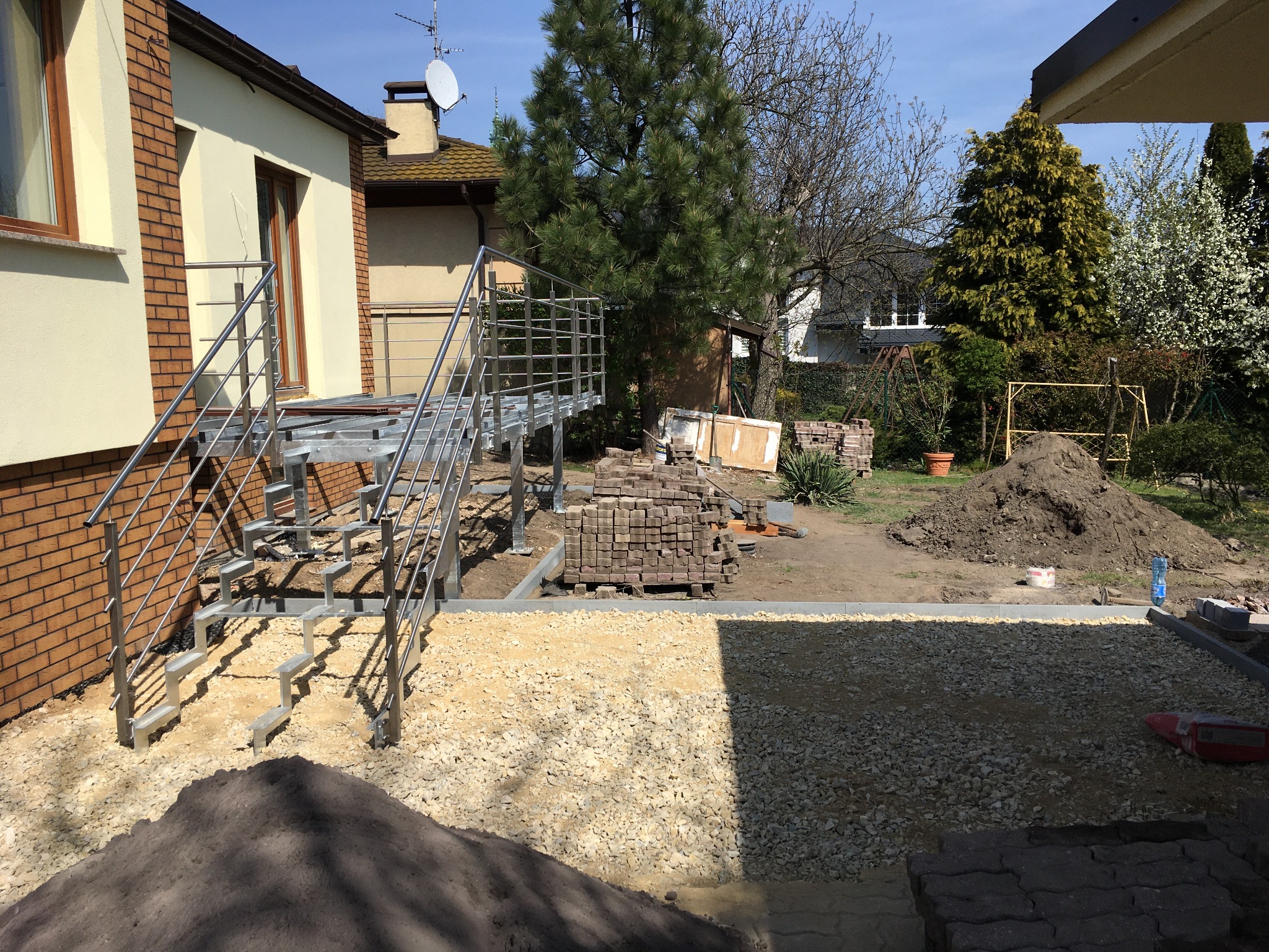 Przygotowanie podłoża pod kostkę brukową w Hucie Starej: wysypany tłuczeń, obrzeża i tymczasowe schody ze stali nierdzewnej.