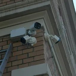 Zewnętrzny montaż trzech kamer monitoringu Hikvision na ceglanej ścianie budynku, widoczna drabina oparta o ścianę.