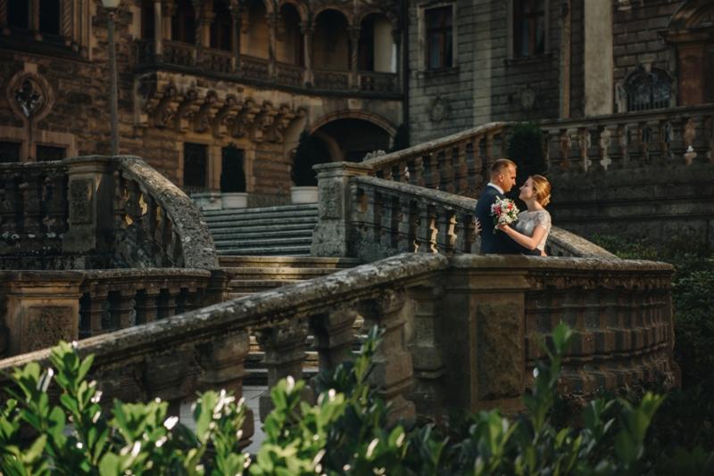 Para młoda w objęciach na tle monumentalnych, kamiennych schodów i zabytkowej architektury zamku, w ciepłym świetle zachodzącego słońca.