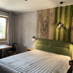 Vitalii Savchenko - Nowoczesna sypialnia z łóżkiem z zielonym zagłówkiem, geometryczną dekoracją jelenia na drewnianej ścianie i pionowymi panelami z mchu dekoracyjnego.