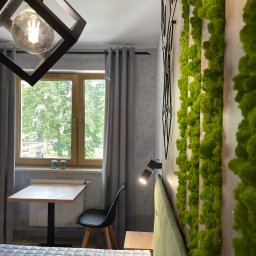 Vitalii Savchenko - Nowoczesna sypialnia z dekoracyjną ścianą z mchu, geometryczną lampą wiszącą, biurkiem przy oknie i minimalistycznym wystrojem.