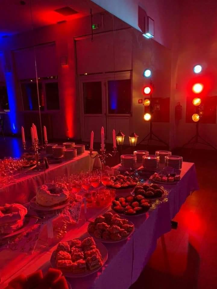 Stół bufetowy z przekąskami i napojami oświetlony czerwonym i niebieskim światłem scenicznym, świeczniki i lampiony dekoracyjne.