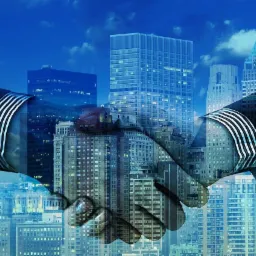 Uścisk dłoni na tle panoramy miasta z wieżowcami, symbolizujący porozumienie biznesowe lub finansowe.