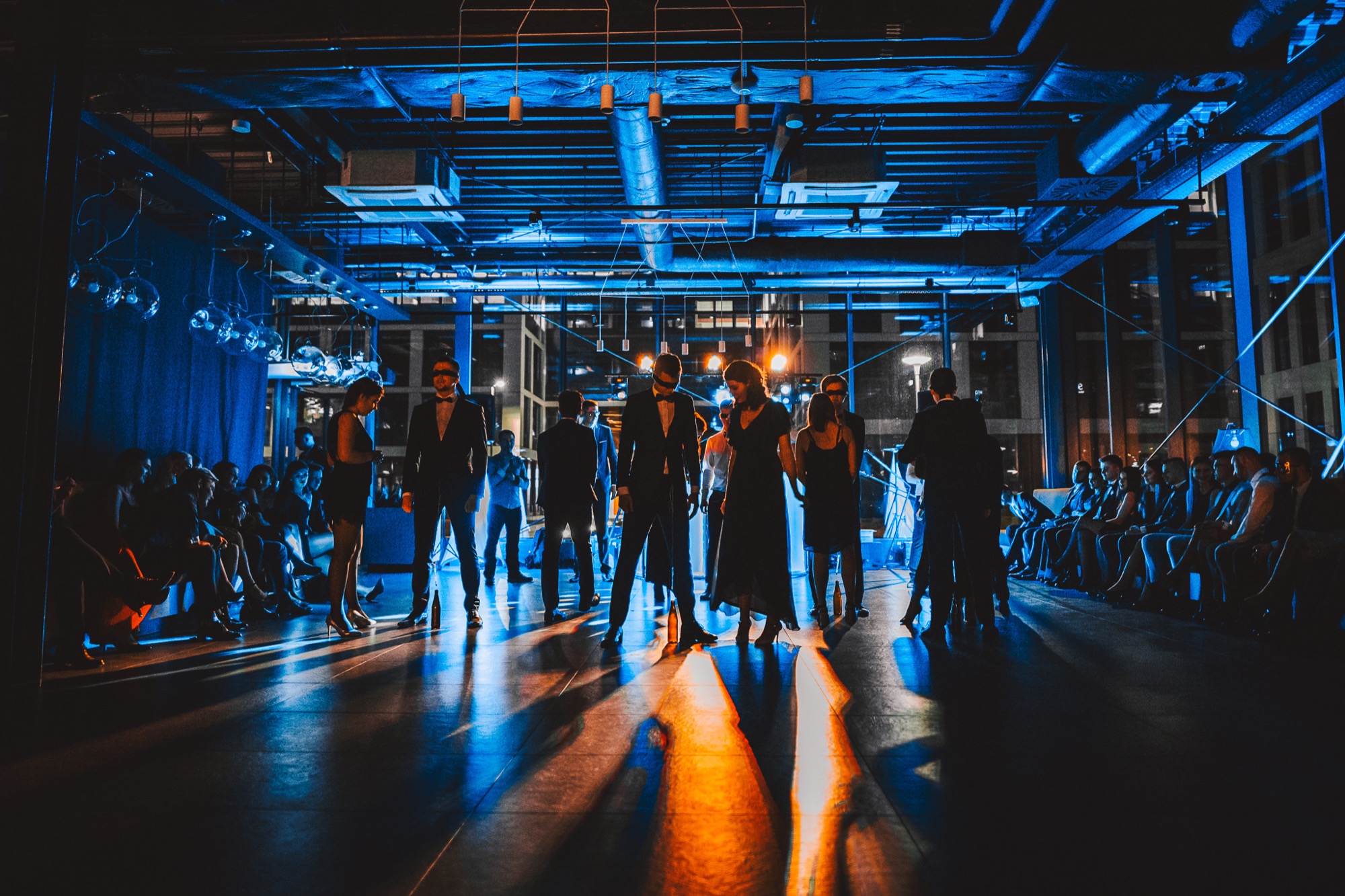 Elegancko ubrani goście na imprezie firmowej w nowoczesnym wnętrzu z industrialnym sufitem i oświetleniem punktowym.