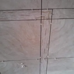 Układanie beżowych płytek z dekoracyjnym pasem, widoczne krzyżyki dystansowe, etap prac wykończeniowych.