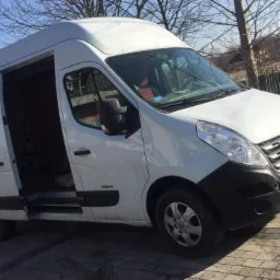 Biały bus Renault Master z otwartymi drzwiami przesuwnymi, zaparkowany na brukowanej powierzchni w słoneczny dzień, z widocznym numerem rejestracyjnym SD 5503F.