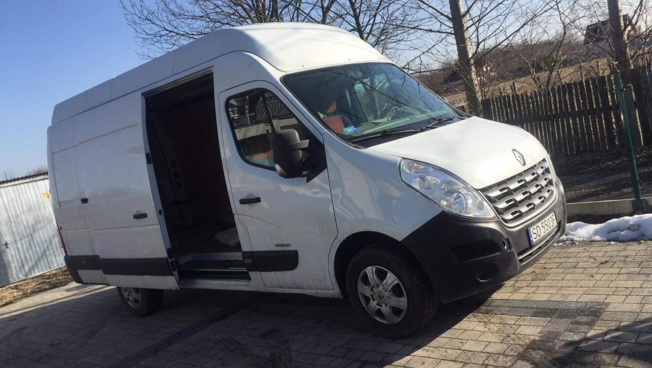 Biały bus Renault Master z otwartymi drzwiami przesuwnymi, zaparkowany na brukowanej powierzchni w słoneczny dzień, z widocznym numerem rejestracyjnym SD 5503F.