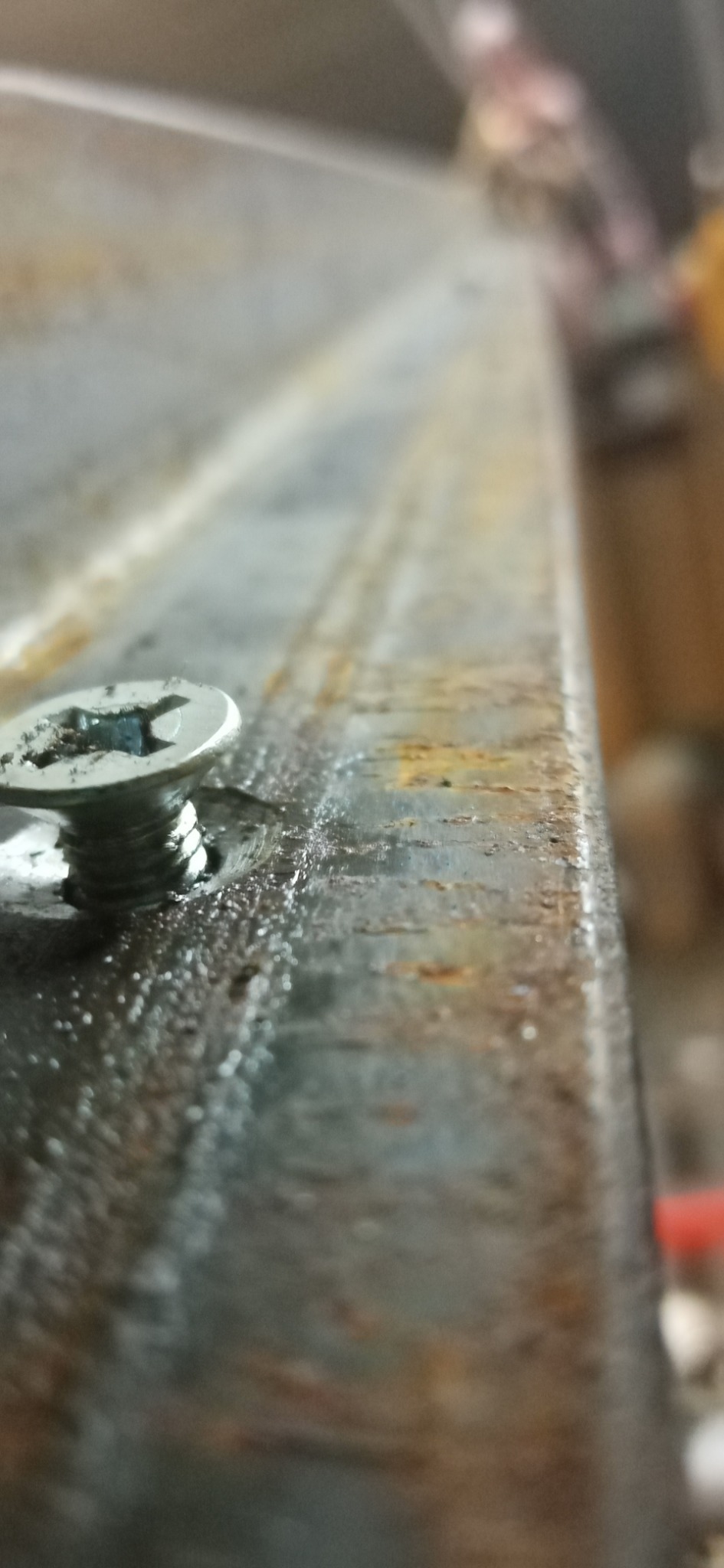 Przybliżenie wkrętu mocującego element metalowy, widoczne ślady rdzy i zabrudzeń na powierzchni.