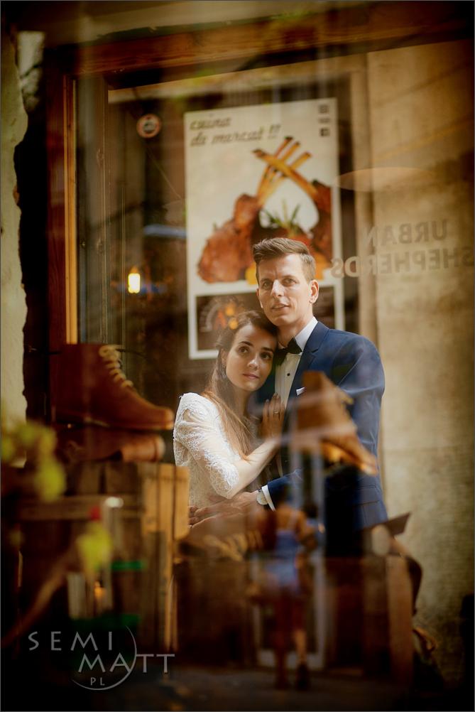 Para młoda w objęciach, odbicie w witrynie sklepu z obuwiem i plakatem gastronomicznym w tle.