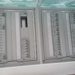 Rozdzielnica elektryczna z zainstalowanymi bezpiecznikami, opisana ręcznie na białych paskach, widoczna w skrzynce z tworzywa sztucznego.