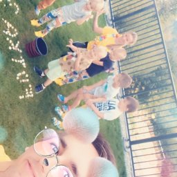 Alan Gruszka - Zdjęcie z filtrem przedstawiające grupę dzieci i opiekuna na trawie, z napisem 'Happy' ułożonym z białych przedmiotów, obok stoi wiaderko.