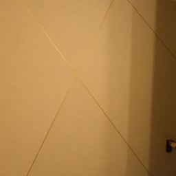 USŁUGI OGÓLNOBUDOWLANE KEN-BUD MACIEJ KĘDZIERSKI - Beżowa ściana z geometrycznym wzorem z cienkich, złotych linii, widoczny fragment schodów i listwa przypodłogowa