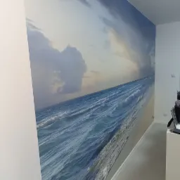 Fototapeta z motywem morza na ścianie w jasnym wnętrzu, widok na fale i pochmurne niebo, subtelne oświetlenie.