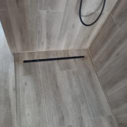 USŁUGI OGÓLNOBUDOWLANE KEN-BUD MACIEJ KĘDZIERSKI - Ułożone panele podłogowe imitujące drewno z czarną listwą przypodłogową i fragmentem kabla w rogu.