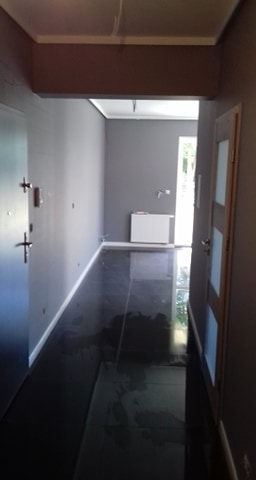 Korytarz w szarościach z błyszczącą, ciemną podłogą, widok z perspektywy wejścia, częściowo otwarte drzwi po prawej stronie.