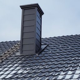 Art-Dach - Nowy, grafitowy komin wentylacyjny z blachy na dachu pokrytym dachówką ceramiczną z resztkami śniegu, widoczne orynnowanie.