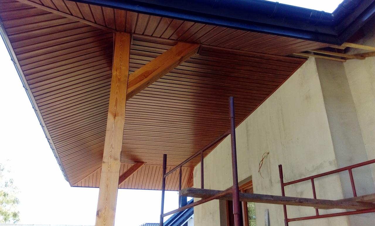 Drewniana podbitka dachowa z widoczną konstrukcją wsporczą i rynną, częściowo zasłonięta przez rusztowanie.