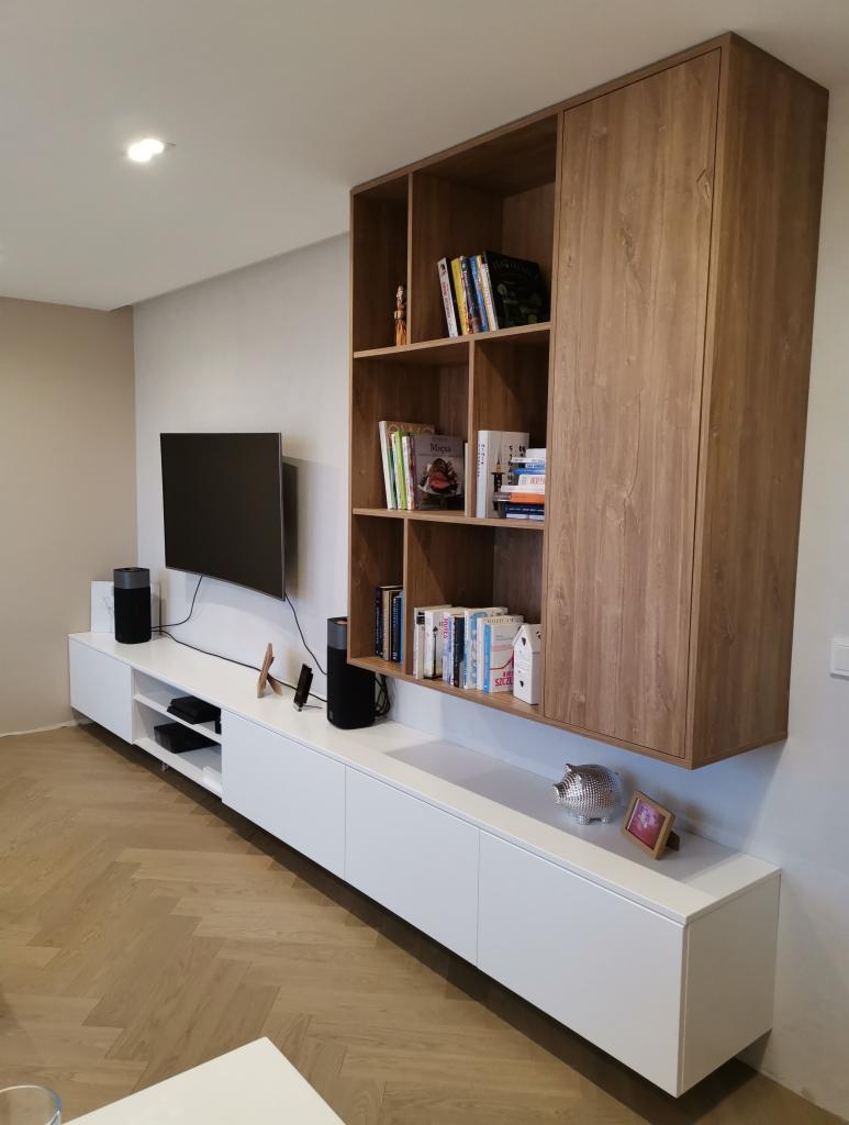 Nowoczesna zabudowa ściany z białymi szafkami dolnymi i drewnianym regałem wiszącym, telewizor na ścianie, parkiet w jodełkę na podłodze.