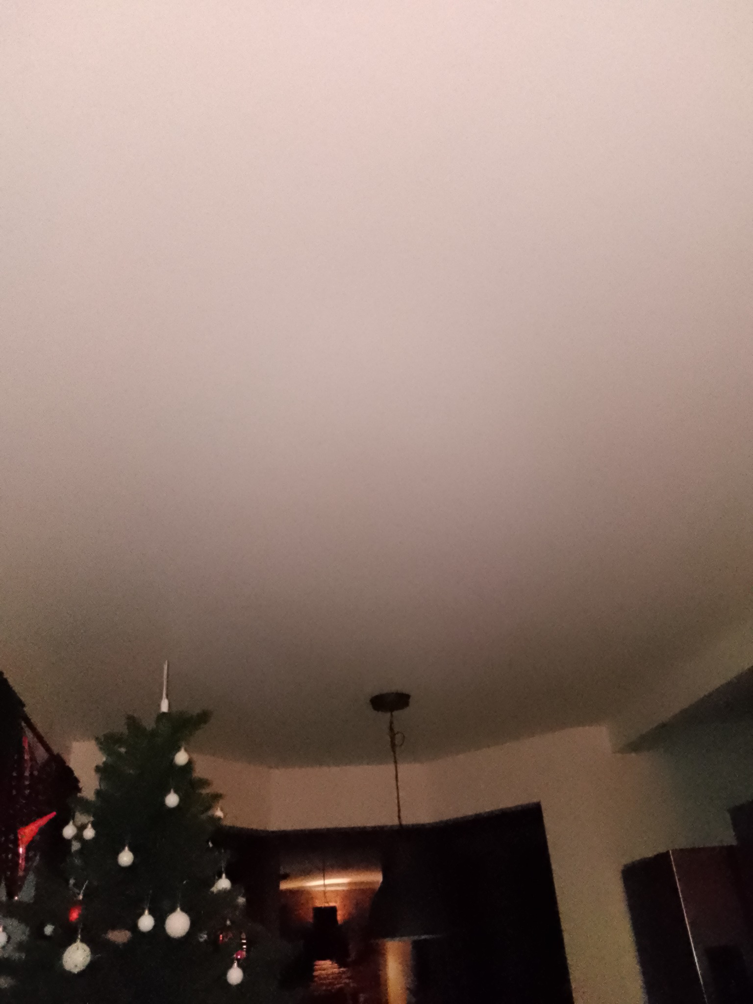 Nisko zawieszony sufit w słabym oświetleniu, widoczny fragment choinki z białymi bombkami i fragment lampy wiszącej.