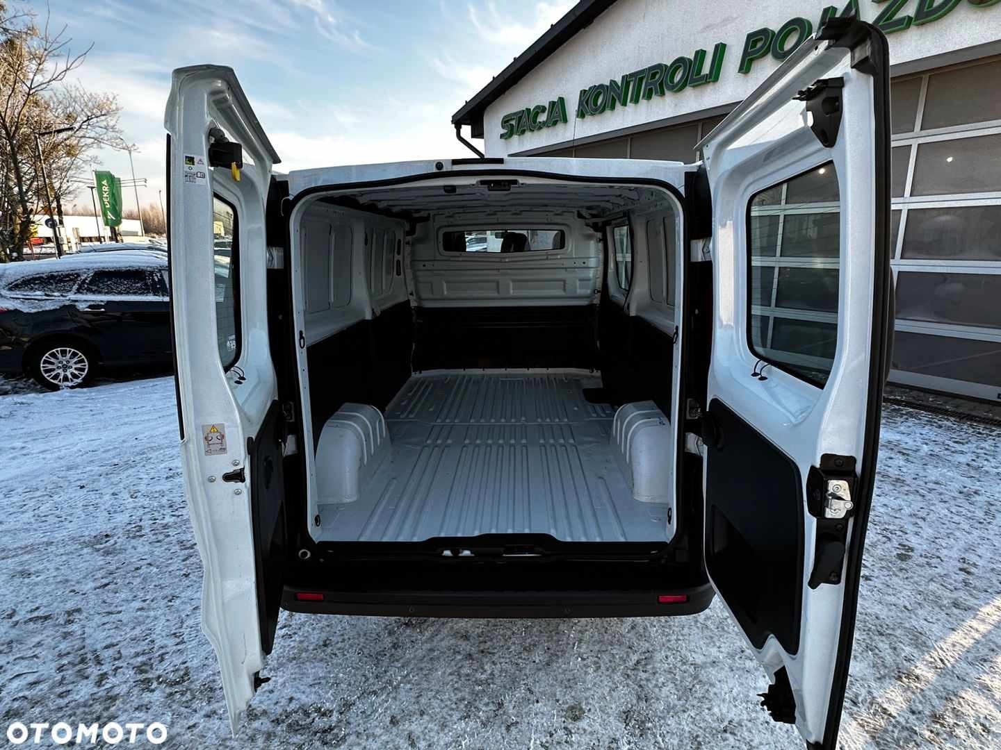 Wnętrze paki białego busa dostawczego z otwartymi drzwiami na zewnątrz na tle ośnieżonego terenu.