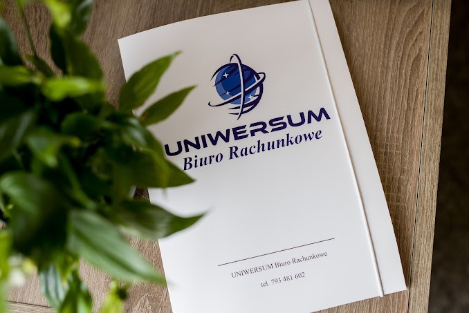 Biała teczka z logo i nazwą 'UNIWERSUM Biuro Rachunkowe' leży na drewnianym biurku obok zielonej rośliny doniczkowej.