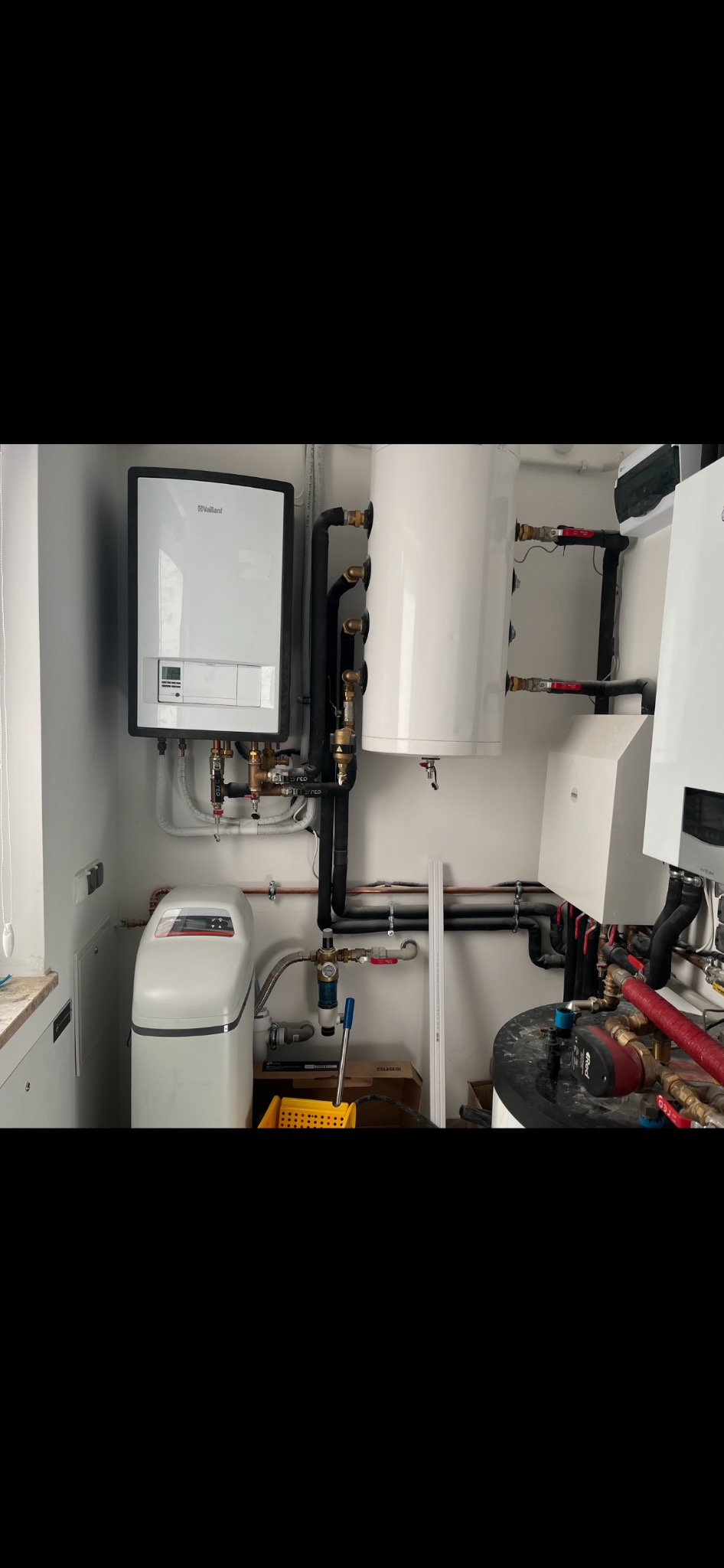 Kotłownia z zamontowanym piecem gazowym marki Vaillant, bojlerem, zmiękczaczem wody i rozbudowaną instalacją hydrauliczną z rurami miedzianymi i czarnymi, widocznymi zaworami i osprzętem.