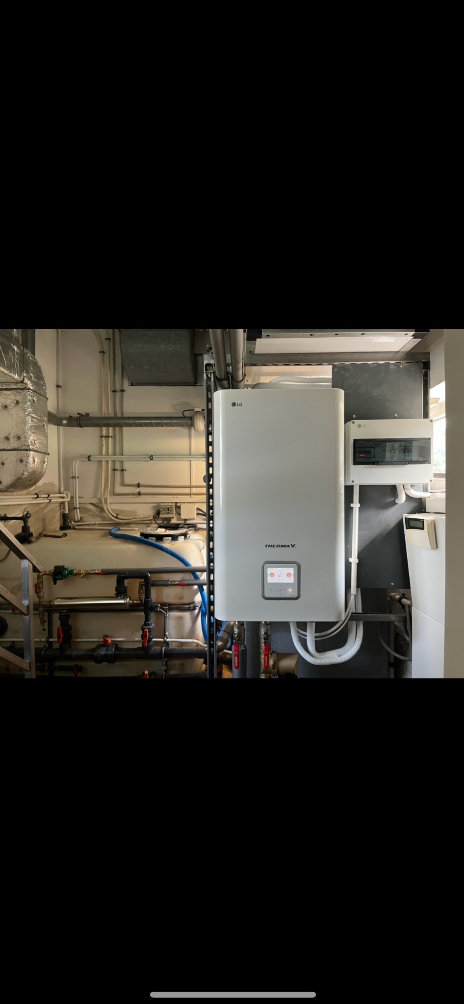 Biała pompa ciepła LG Therma V zamontowana w pomieszczeniu technicznym, widoczne rury, zawory i zbiornik buforowy.