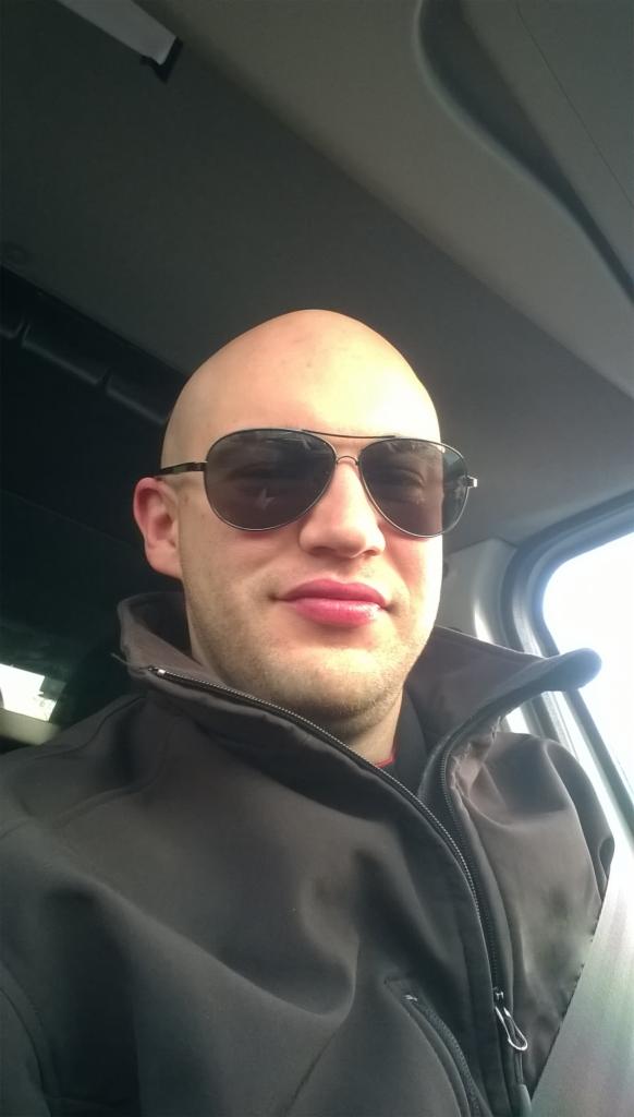 Autoportret mężczyzny w okularach przeciwsłonecznych, siedzącego w samochodzie z zapiętym pasem bezpieczeństwa.