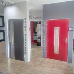 Ekspozycja dwóch modeli drzwi w salonie w Lęborku: szare drzwi z podświetleniem LED oraz czerwone drzwi z centralnym przeszkleniem, oba modele z napisem 'Drzwi Standard' na ościeżnicy.