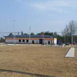 WM BUDSTAR Sp.z o.o . Sp.k. - Budynek stacji transformatorowej z pomalowaną elewacją w biało-pomarańczowe pasy, widoczna wieża telekomunikacyjna w tle, teren przygotowany pod inwestycję.