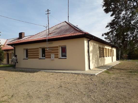 Budynek po renowacji elewacji, z beżową fasadą, brązowymi akcentami okiennymi i czerwoną dachówką, widoczny mężczyzna w tle.