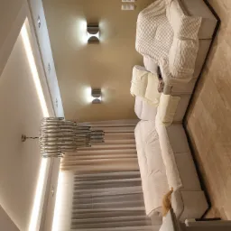 Nowoczesny salon z długą, jasną sofą, szklanym żyrandolem i oświetleniem punktowym, widziany z perspektywy sufitu.