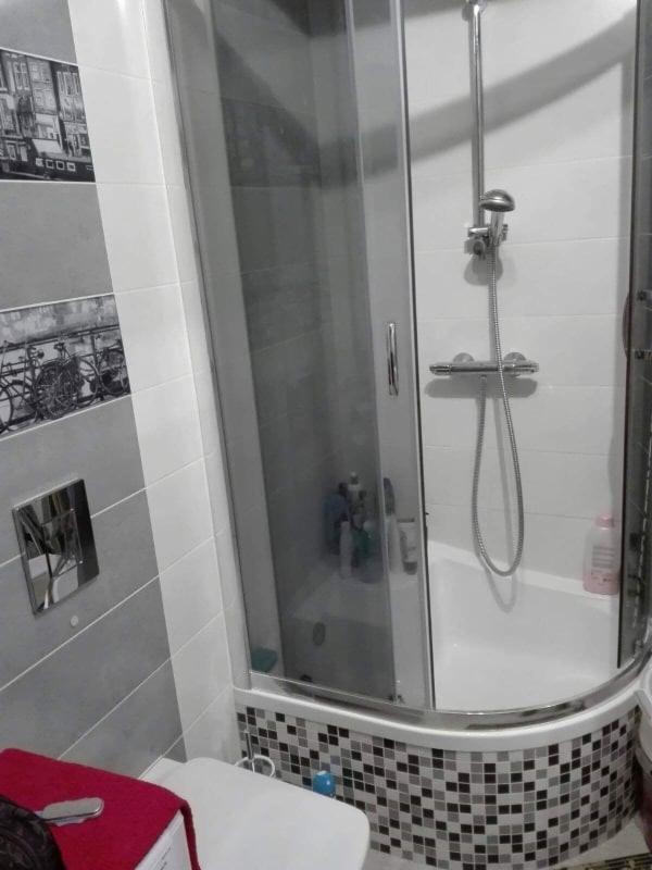 Wykończona łazienka z kabiną prysznicową z hydromasażem, obudowaną mozaiką w odcieniach szarości i czerni, oraz szarymi i białymi płytkami ze wzorem roweru na ścianie.