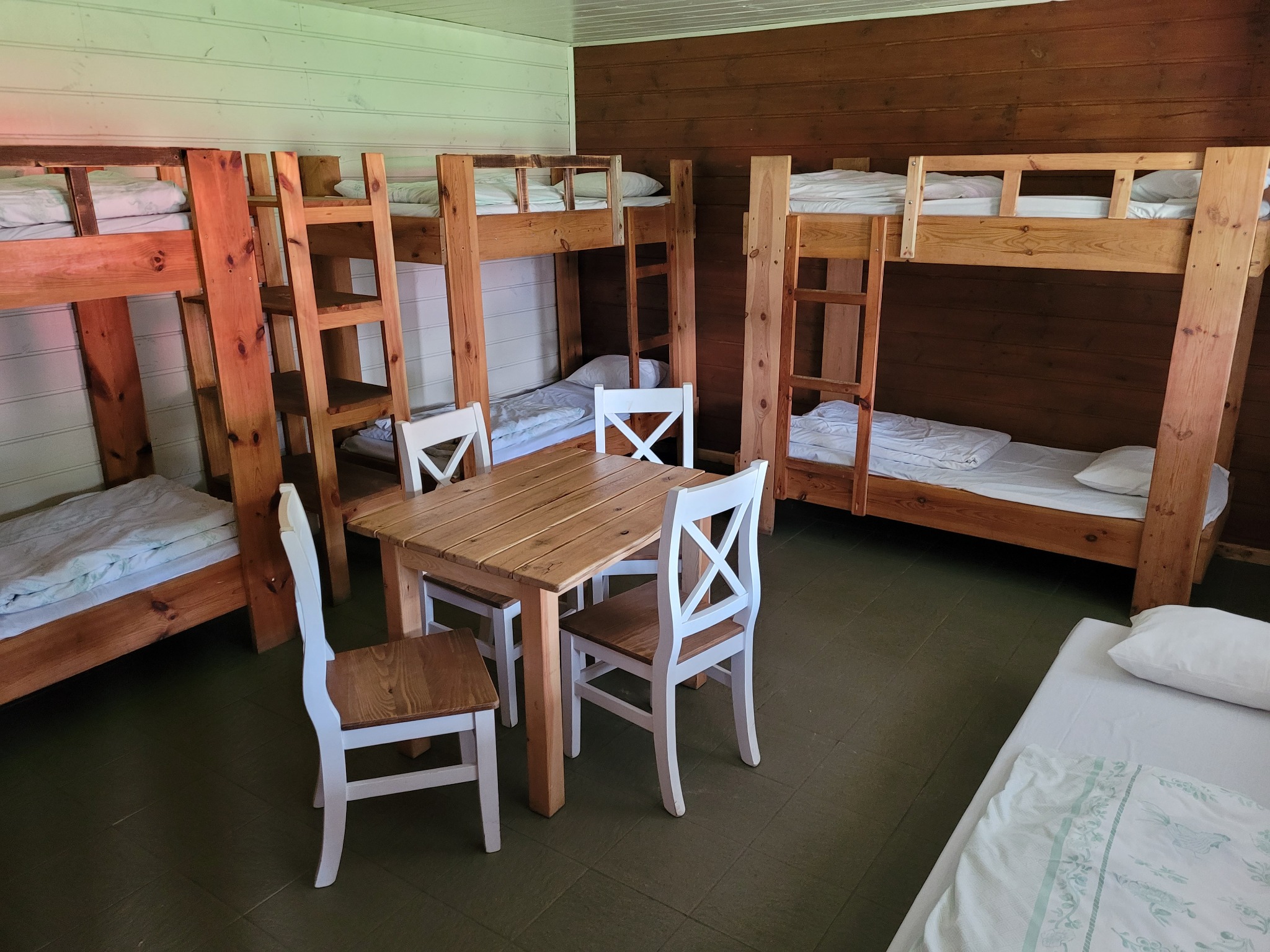 Wnętrze pokoju z drewnianymi łóżkami piętrowymi, stołem i krzesłami, w stylu skandynawskim.