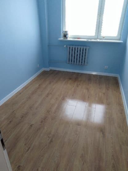 Pusty pokój po remoncie, z panelami podłogowymi w odcieniach brązu, błękitnymi ścianami i grzejnikiem pod oknem.