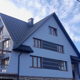 F.H.U CIESIELSKI PIOTR - Dwupiętrowy dom z ciemnoszarym dachem dwuspadowym i jasnoniebieską elewacją z dekoracyjnymi szarymi pasami i kamienną podmurówką, uchwycony pod kątem z dołu.