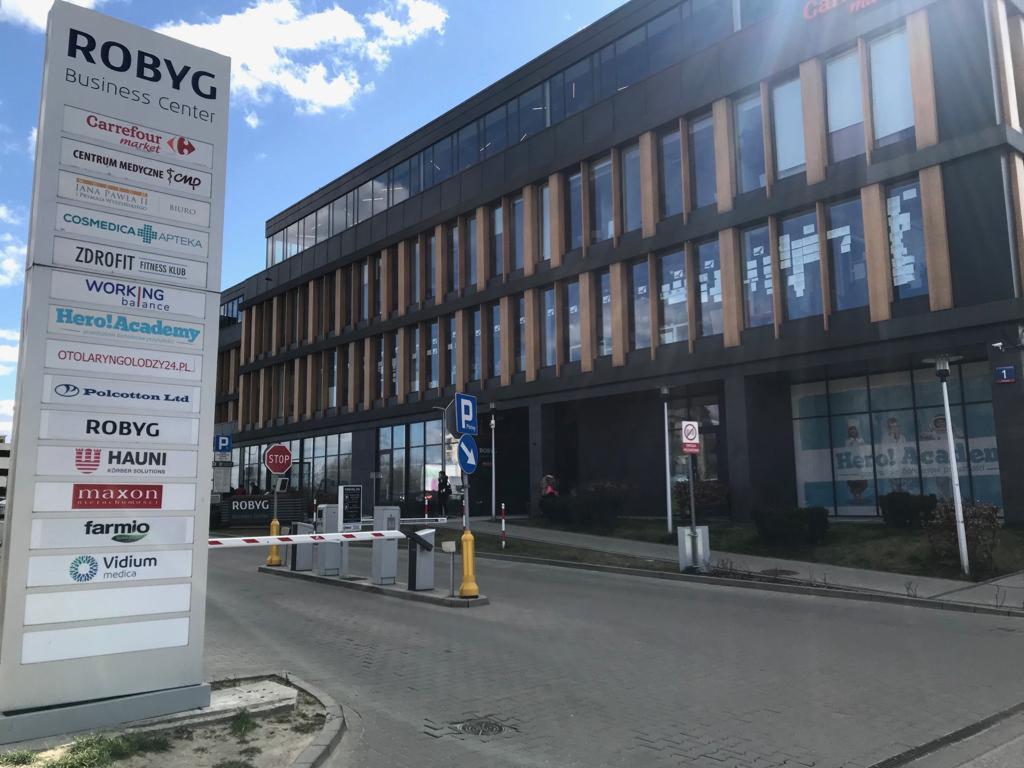 Zewnętrzny widok nowoczesnego biurowca ROBYG Business Center z tablicą informacyjną zawierającą listę firm i usługodawców, w tym centrum medyczne CMP i gabinet otolaryngologiczny, z widocznymi...