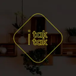 Grafika z żółtym neonowym logo 'i tak i tak' na tle ściany z drewnianymi półkami, na których stoją rośliny i dekoracyjne butelki.