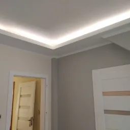 Nowoczesny sufit podwieszany z oświetleniem LED w narożniku pokoju, widoczne dwie ściany pomalowane na różne odcienie szarości, białe drzwi z przeszkleniami.