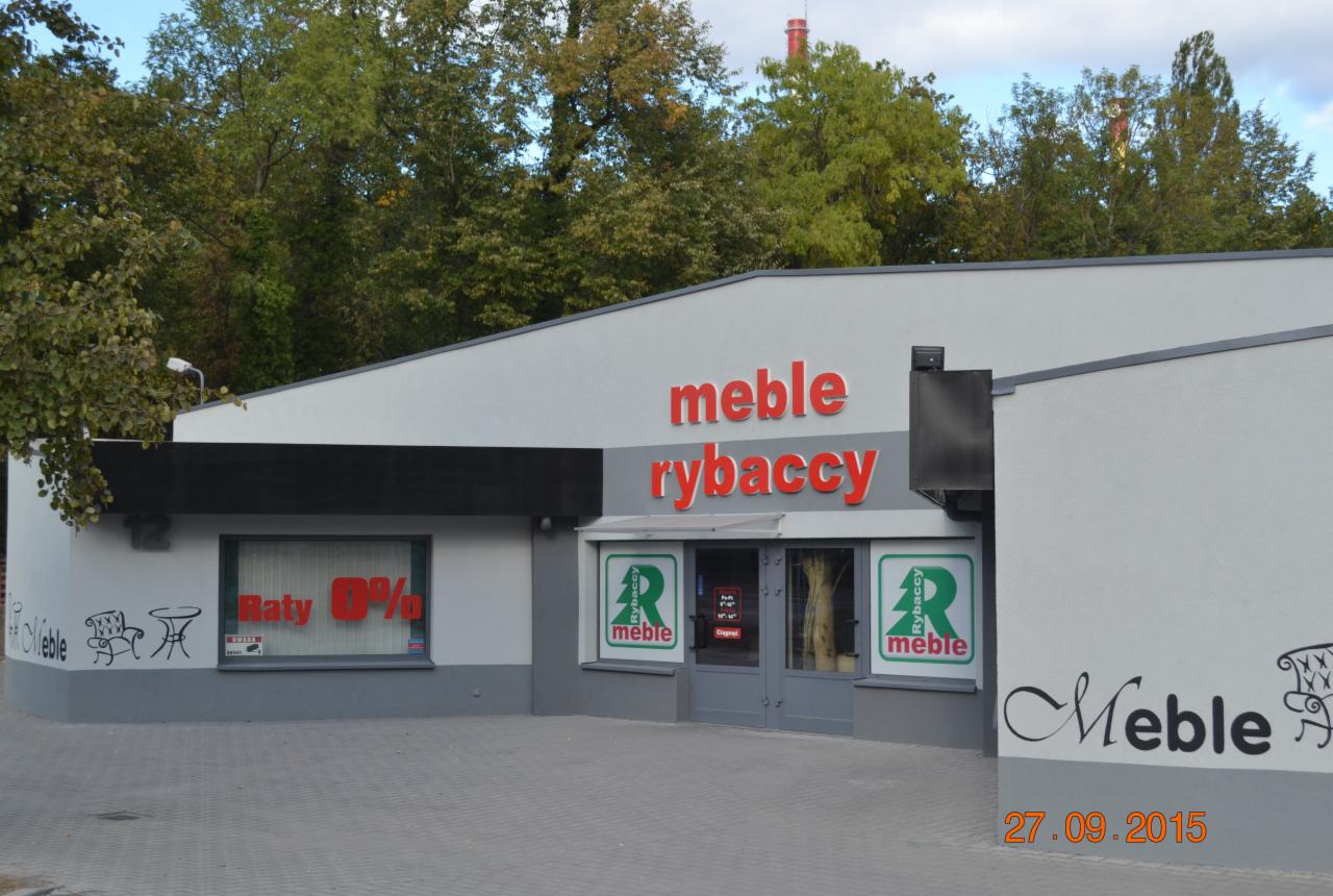 Fasada budynku sklepu meblowego z napisem 'meble rybaccy' w kolorze czerwonym, widoczne okno z napisem 'Raty 0%' oraz rysunki mebli na ścianie.