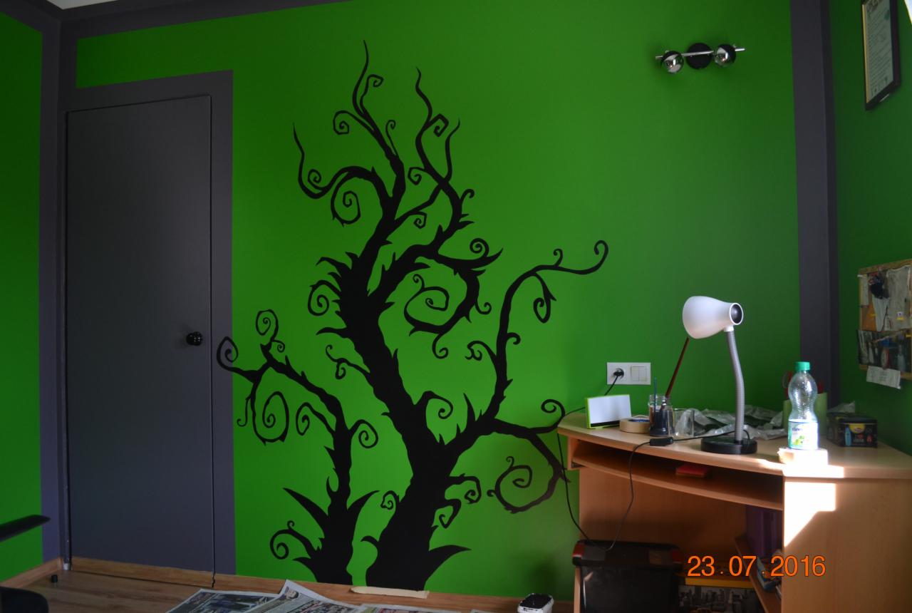 Czarny, abstrakcyjny motyw drzewa namalowany na jaskrawo zielonej ścianie pokoju, widoczny fragment biurka z lampką i akcesoriami.