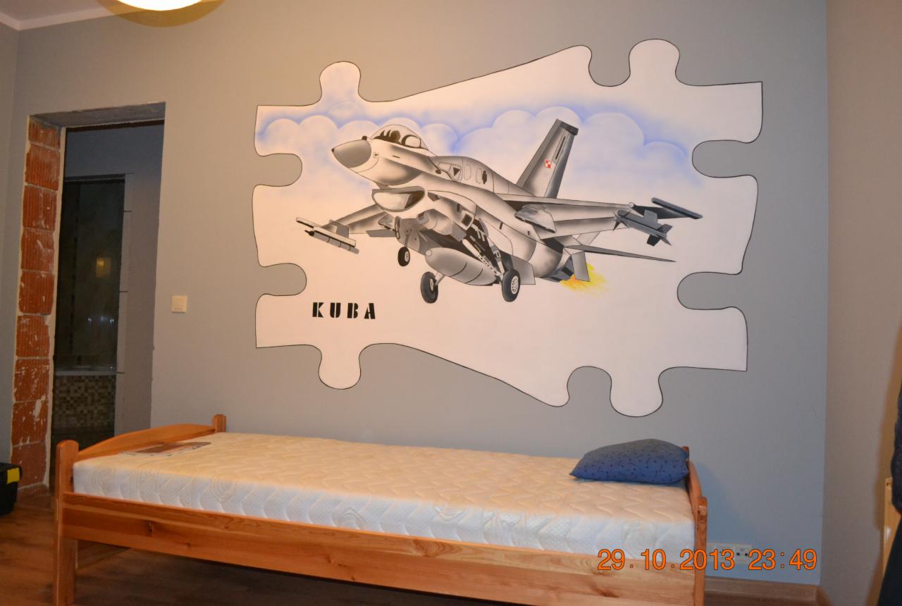 Pokój dziecięcy z łóżkiem i malowidłem na ścianie przedstawiającym samolot w kształcie puzzla z imieniem 'KUBA'.