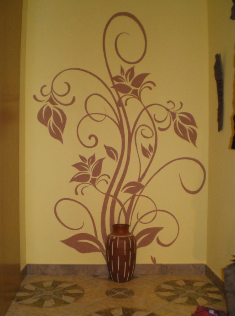 Dekoracyjny motyw roślinny w kolorze brązowym, namalowany na żółtej ścianie w rogu pokoju, z brązowym wazonem na podłodze.