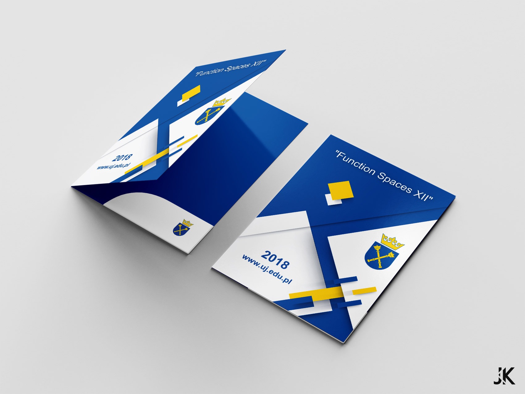 Dwie otwarte, niebiesko-białe teczki z logo Uniwersytetu Jagiellońskiego i napisem 'Function Spaces XII' leżące na szarym tle.
