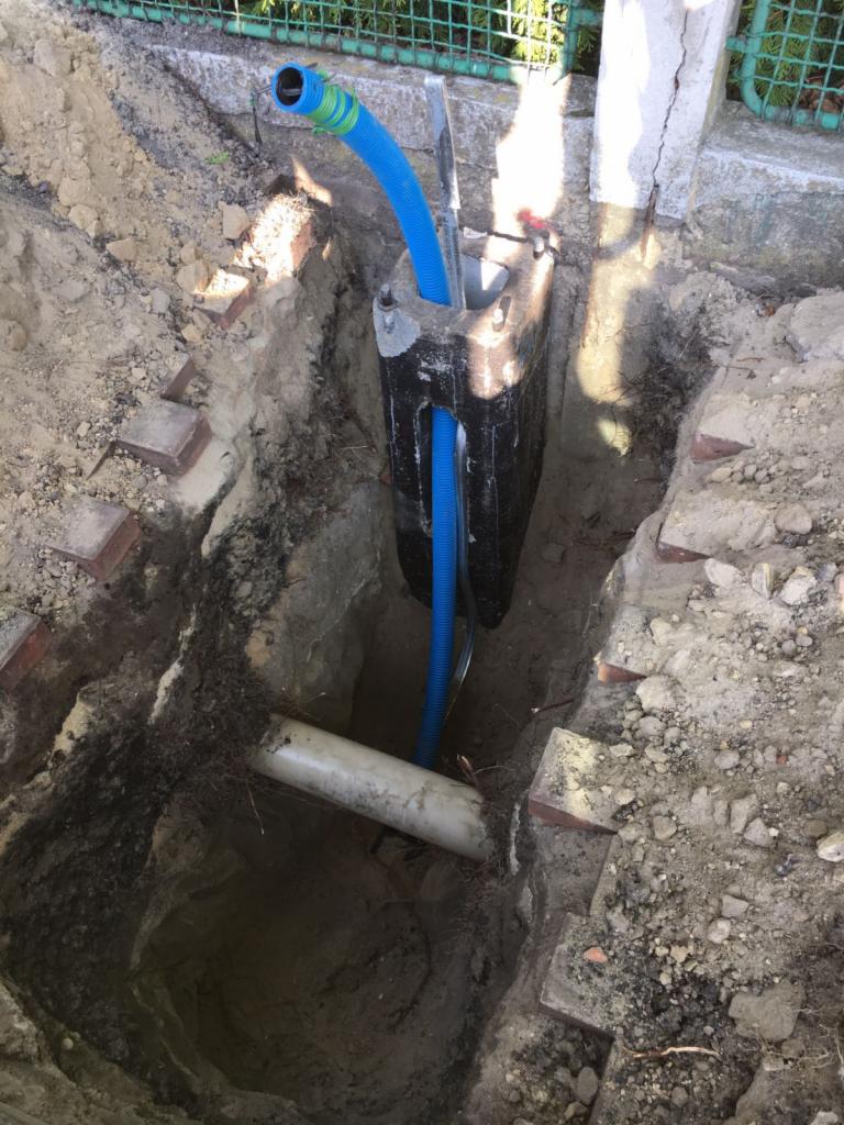 Wykop z widocznymi przewodami w peszlu, częściowo zabezpieczony betonową konstrukcją, z fragmentami cegieł na krawędzi wykopu.