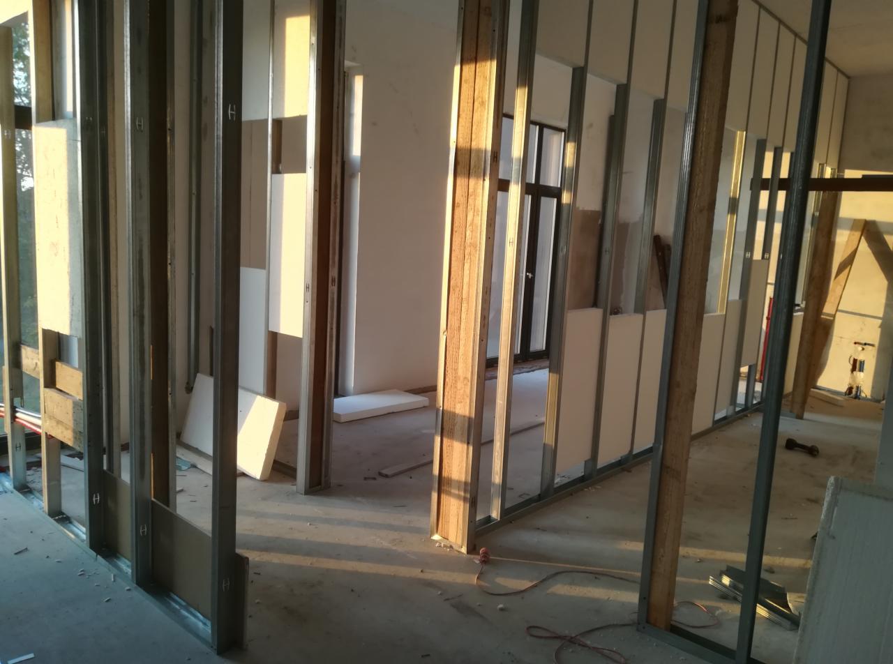 Konstrukcja ścian działowych z profili stalowych i częściowo zamontowanych płyt karton-gips, widoczne okno w tle i przewody elektryczne na podłodze.