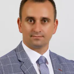 Portret mężczyzny w niebieskiej marynarce w kratę i wzorzystym krawacie, patrzącego wprost.