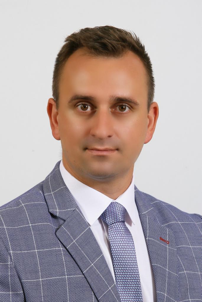 Portret mężczyzny w niebieskiej marynarce w kratę i wzorzystym krawacie, patrzącego wprost.