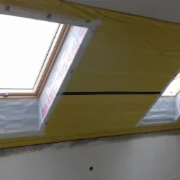 Dwa okna dachowe w trakcie montażu, zabezpieczone folią ochronną i taśmą malarską, żółta folia paroizolacyjna na poddaszu.